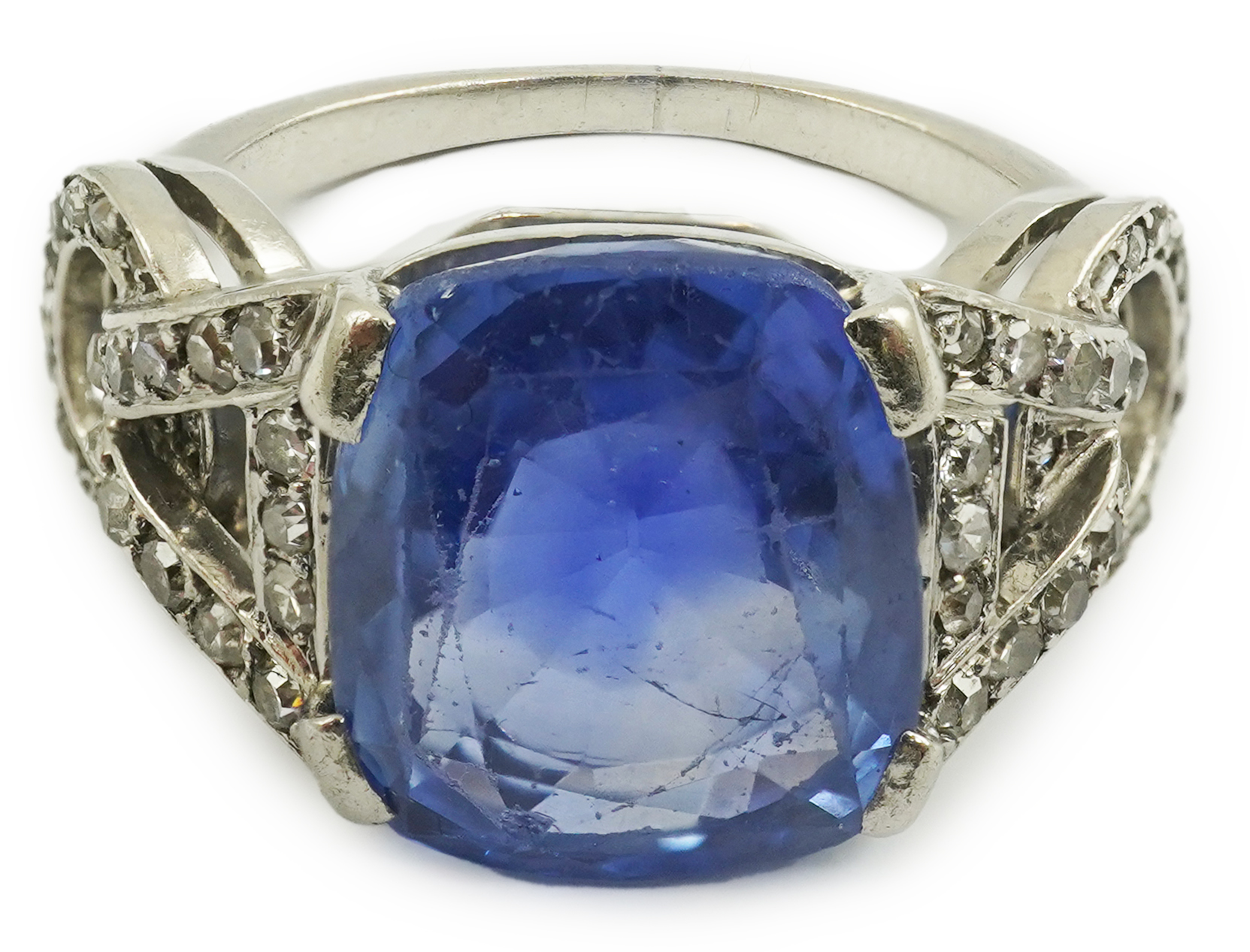 A mid to late 20th century platinum and single stone tapered cushion cut sapphire set dress ring, with diamond chip set pierced shoulders